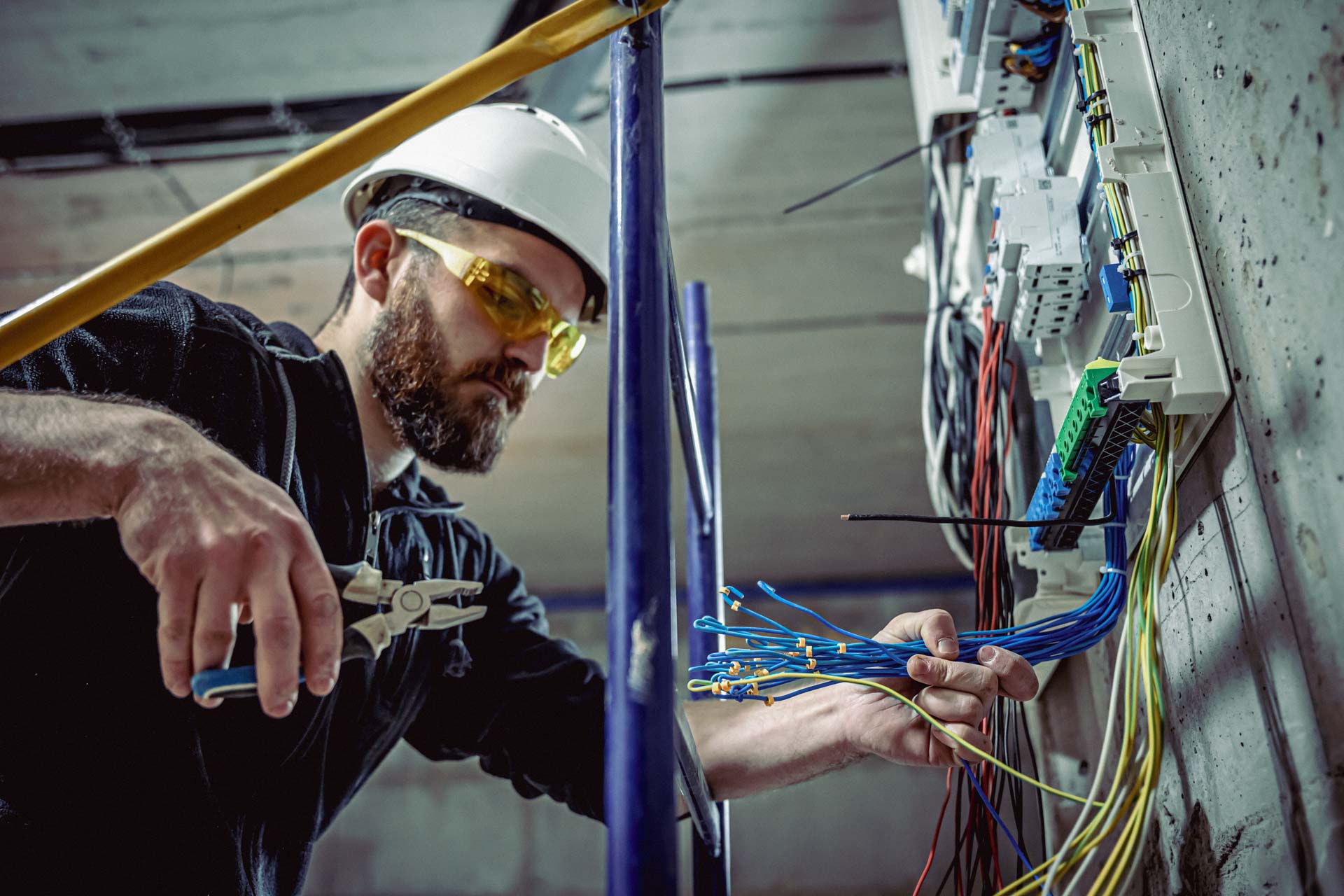 A Male Electrician Works In A Switchboard With An Electrical Connecting Cable.